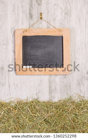 A wooden framed blackboard with chalk hanging on a rustic background with straw grass and copy space for your text or picture