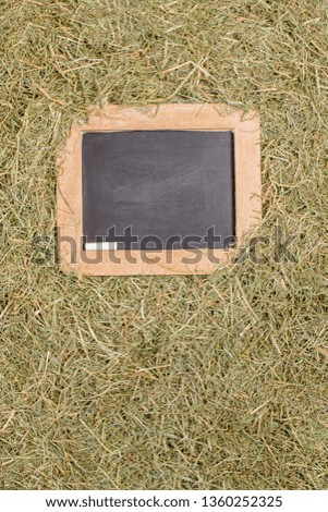 A wooden framed blackboard with chalk surrounded by dried straw grass with copy space for your text or picture
