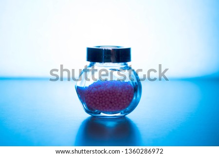 Glass jar with pink small balls on a blue background.