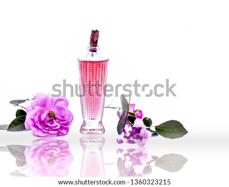Rose flower with its extracted spray or perfume in a transparent glass bottle isolated on white along with rose petals.