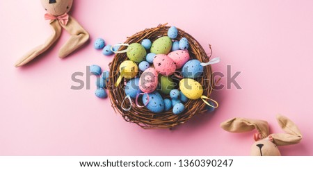 Colorful decor easter eggs in a nest and bunnies on pastel pink background. Flat lay