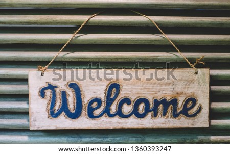 Rustic wood welcome sign hanging by rope on antique door. Greeting signboard.