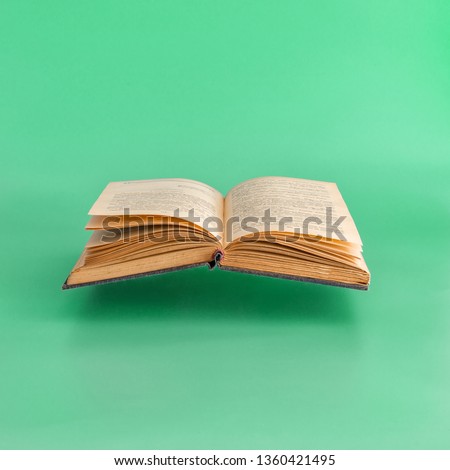 Levitating open old book on green background.  Minimal concept. Copy space Royalty-Free Stock Photo #1360421495