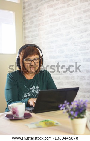 Senior Woman Using Laptop On Desk At Home. The elderly lady with glasses intently browses the internet content on a laptop. Vertical. Toned picture.