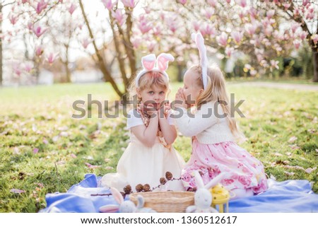 Little cute girls are sitting on the grass near the mogolia. Girls in costumes Easter bunnies. Spring.