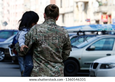 Woman in uniform carries a child in her arms. Protect the child. Child custody service Royalty-Free Stock Photo #1360546331