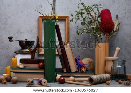 A group of various items: books,spools with thread,a safety pin,beads,a hook,a skein of line,candles,a deer horn,a mortar,a glass jar with coffee beans,a coffee mill,a frame & sprigs with flowers etc.