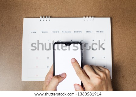 Male hand using touch screen smart phone device mock up with blank screen isolated on wooden background. Checking schedule on smart phone. Can be use for article of business, travel, holiday Royalty-Free Stock Photo #1360581914