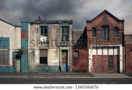 derelict abandoned houses and buildings on a deserted residential street with boarded up windows and decaying crumbling walls against a grey cloudy sky Royalty-Free Stock Photo #1360586876