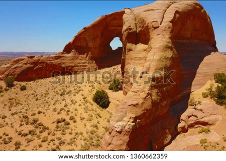 Large rock in Utah with hole in center. Taken on bright blue day by drone, hosting myself, a climber, on a small cliff edge.