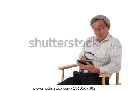 A old Asian man sitting on a chair enjoy using tablet with magnify glass on isolated white background.