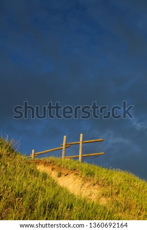 A hill is lit by golden-hour sunlight with dark storm clouds in the background