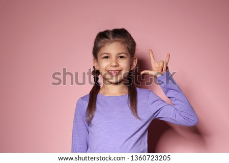 Little girl showing I LOVE YOU gesture in sign language on color background