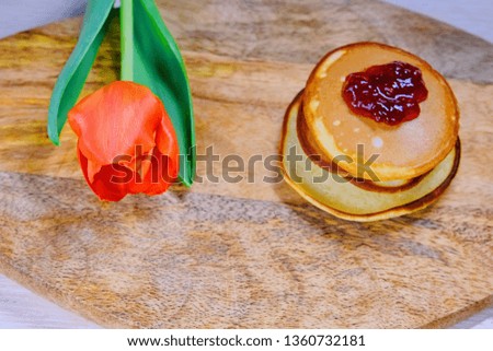 Pancakes with jam and Tulip. A red flower lies next to the pastries on the kitchen Board. A hill of fresh pancakes on the table in spring.
