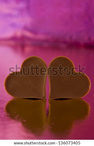 Photograph of two chocolate hearts on a pink background.