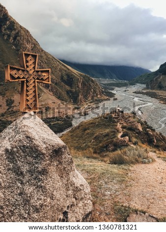 Amazing view Georgian military road, high in the Caucasus autumn mountains. Summer time, high peak ridge. Wooden catholic monument cross pass on the big stone beside Mountain green valley gorge 