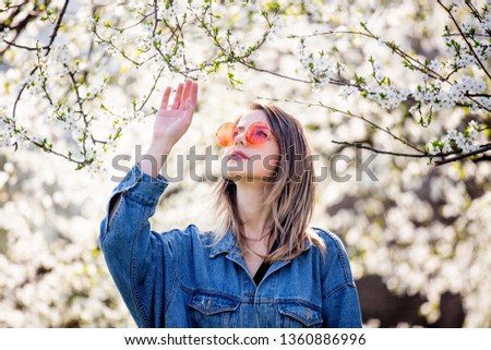 Young girl in a denim jacket and sunglasses stands near a flowering tree in the park. Spring season