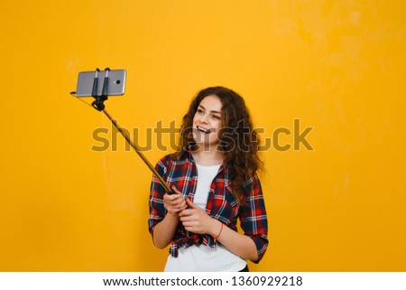 Portrait a brunette girl who makes her selfie and smiles on a yellow background