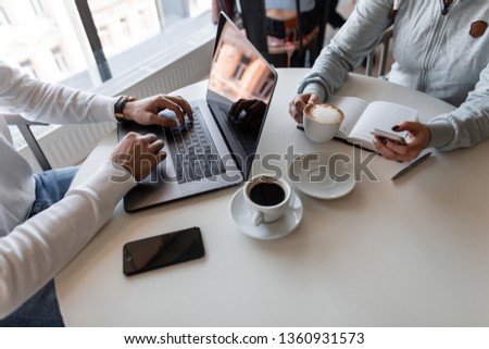 Successful business woman listens to a colleague drinks coffee and looks into the phone. Two business people discuss working moments while sitting at a table in a cafe. Remote work. View from above.