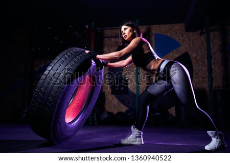 Attractive fit middle age woman athlete working out with a huge tire, turning and flipping in the gym. woman exercising with big tire.