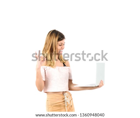 Pretty blonde teenager girl doing an ok gesture with her hand while holding a laptop against a white background