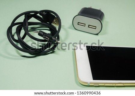 a mobile phone in the middle of black usb cable with different point ends and block adapter on green background. Keep the battery charged on your device anyway you go. Tehnology connect close up.