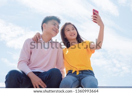 Asian teenager girl and boy smiling while taking their picture by smartphone