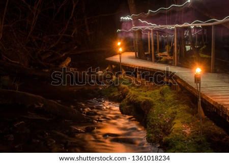 Wooden boards trail with torched torches along the rapid spring river at the night, Latvia