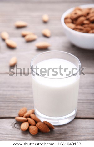 Almond milk in glass with almonds on grey background