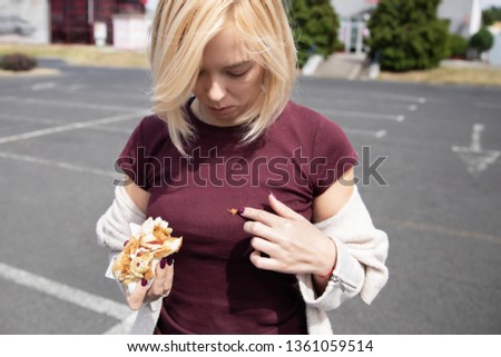 Young beautiful girl eating hot dog in the parking lot. Soiled clothes because of inaccuracy. Royalty-Free Stock Photo #1361059514