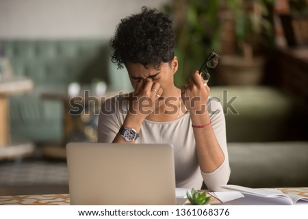 Overworked tired african female student worker holding glasses feel eye strain fatigue after computer work, mixed race woman suffer from pain in dry irritated eyes, bad blurry vision eyesight problem Royalty-Free Stock Photo #1361068376