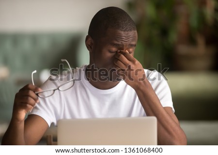 Stressed tired from computer work african american man feeling pain fatigue dry irritated eye strain taking off glasses, sad overworked black man suffer from blurry vision headache weak sight problem Royalty-Free Stock Photo #1361068400