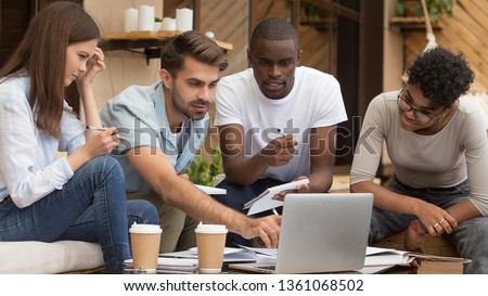 Serious diverse friends study together with laptop and notebooks prepare for exam in cafe, focused multiracial young people group talking using computer sitting on coffee house terrace doing research Royalty-Free Stock Photo #1361068502