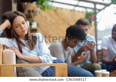 Upset annoyed offended teen girl feel lonely jealous frustrated sit alone in cafe apart of diverse friends obsessed with gadgets, bored sad student ignoring mates lost in phones, mobile addiction  Royalty-Free Stock Photo #1361068517