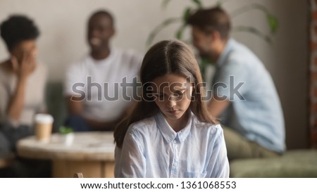 Upset offended bullied young girl sitting alone in cafe, depressed sad lonely teen student excluded by bad friends, female outcast introvert feeling hurt outsider loser suffer from unfair attitude Royalty-Free Stock Photo #1361068553