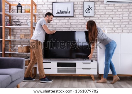 Side View Of Young Couple Lifting Television At Home