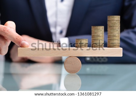 Close-up Of A Businessperson Balancing Increasing Stacked Coins With Finger On Seesaw Royalty-Free Stock Photo #1361081297