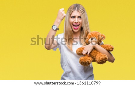 Young beautiful blonde woman holding teddy bear over isolated background annoyed and frustrated shouting with anger, crazy and yelling with raised hand, anger concept
