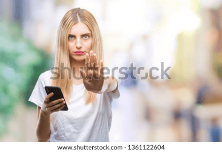 Young beautiful blonde woman using smartphone over isolated background with open hand doing stop sign with serious and confident expression, defense gesture