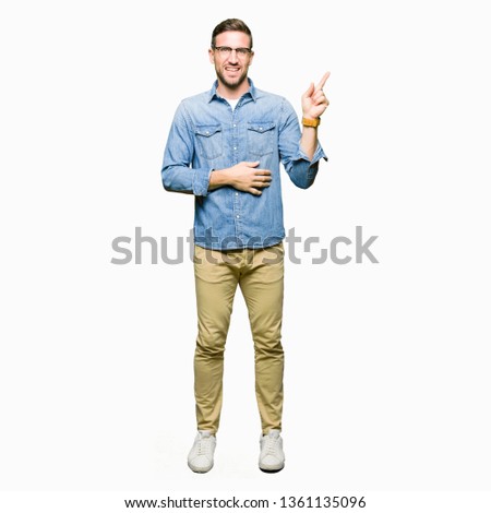 Handsome man wearing glasses with a big smile on face, pointing with hand and finger to the side looking at the camera.