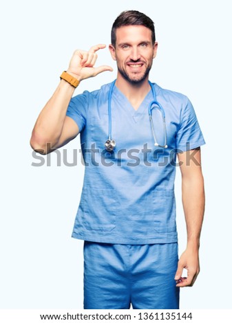 Handsome doctor man wearing medical uniform over isolated background smiling and confident gesturing with hand doing size sign with fingers while looking and the camera. Measure concept.