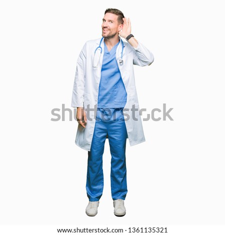 Handsome doctor man wearing medical uniform over isolated background smiling with hand over ear listening an hearing to rumor or gossip. Deafness concept.