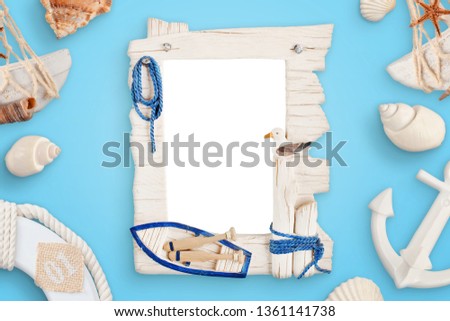 Summer sea travel photo frame on blue desk surrounded with shells, boat anchor, lifebelt.