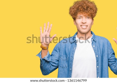 Young handsome man with afro hair wearing denim jacket showing and pointing up with fingers number ten while smiling confident and happy.