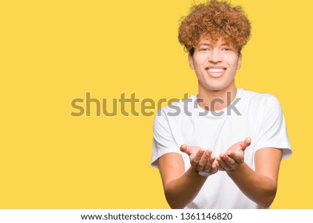 Young handsome man with afro hair wearing casual white t-shirt Smiling with hands palms together receiving or giving gesture. Hold and protection