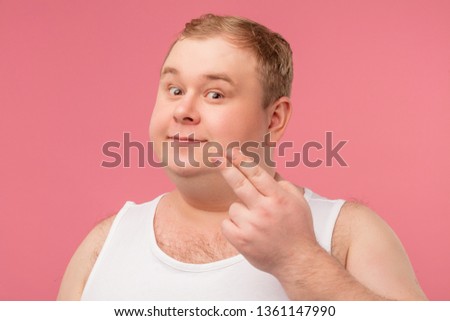 Funny glad jouful man in undershirt applying tonic by cotton pad on face isolated on pink studio background. Hygiene concept, cosmetical goods for skin care