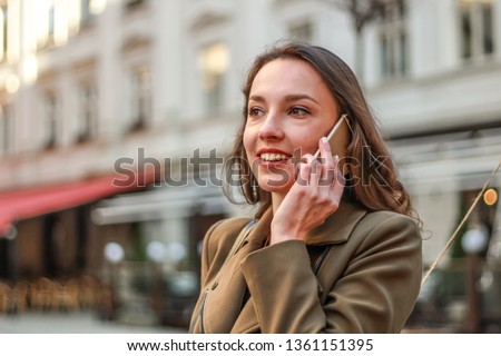 Portrait of a pretty young business lady is negotiating on the phone walking on street. The girl uses gadgets. Lifestyle photos. Stylish clothes