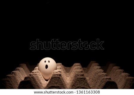 Egg with face on a carton and neutral background black. Conceptual image Free space to write. Humanization of objects.