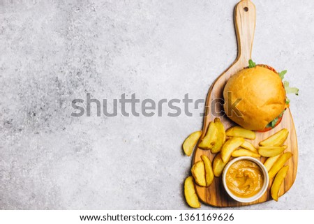 An american burger with fried potatoes on on a wooden cutting board