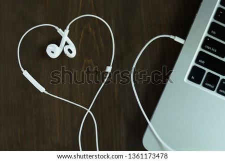 White earphone in heart shape on wooden table by laptop